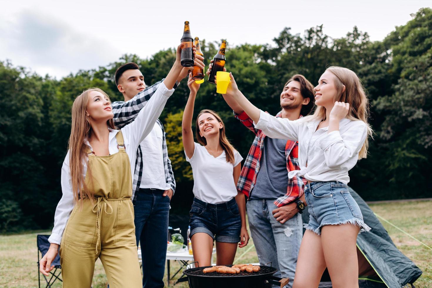 una compañía de amigos levantando botellas con una cerveza en el camping. - imagen foto