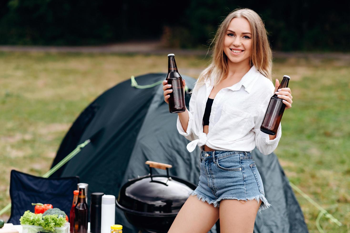 Woman standing and holding a beer in the camping photo