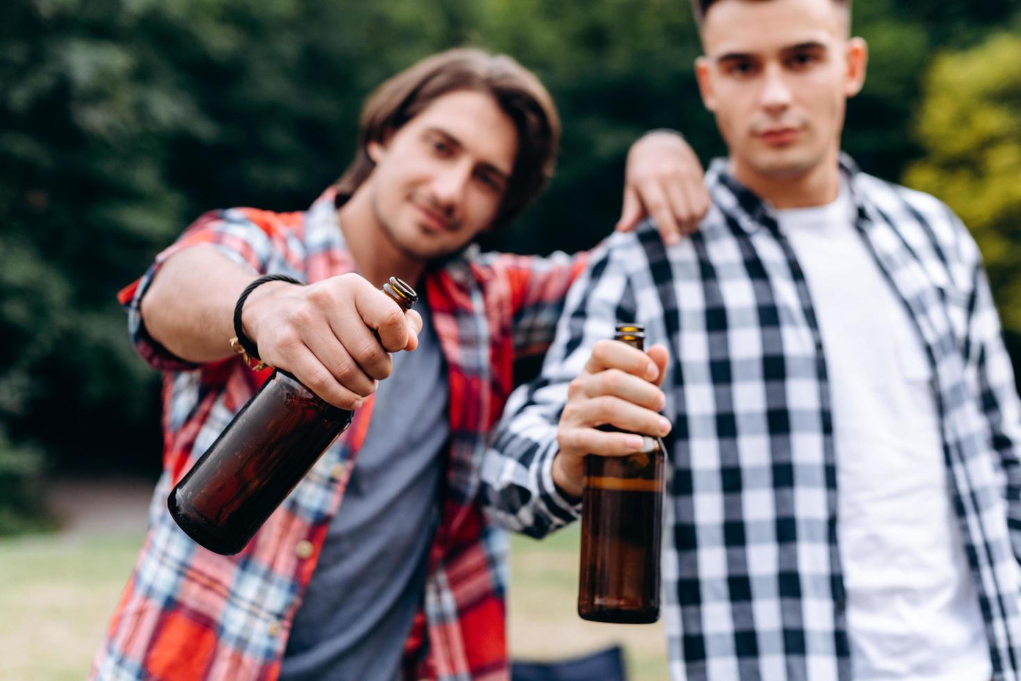 Two guys holding a beer and showing it in the camera in the camping . - Image photo