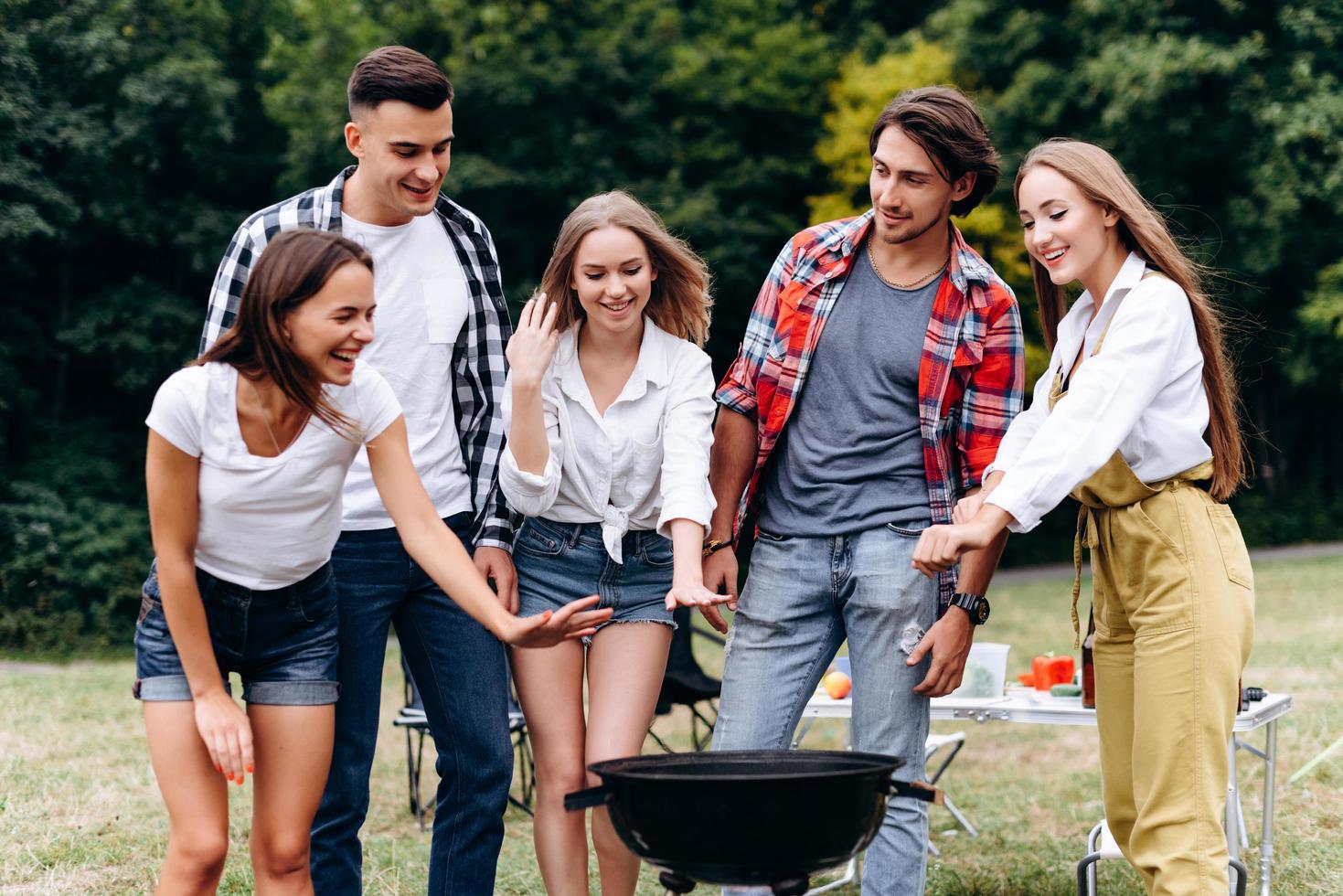 una compañía de amigos se divierte en el campamento de pie junto a la barbacoa foto