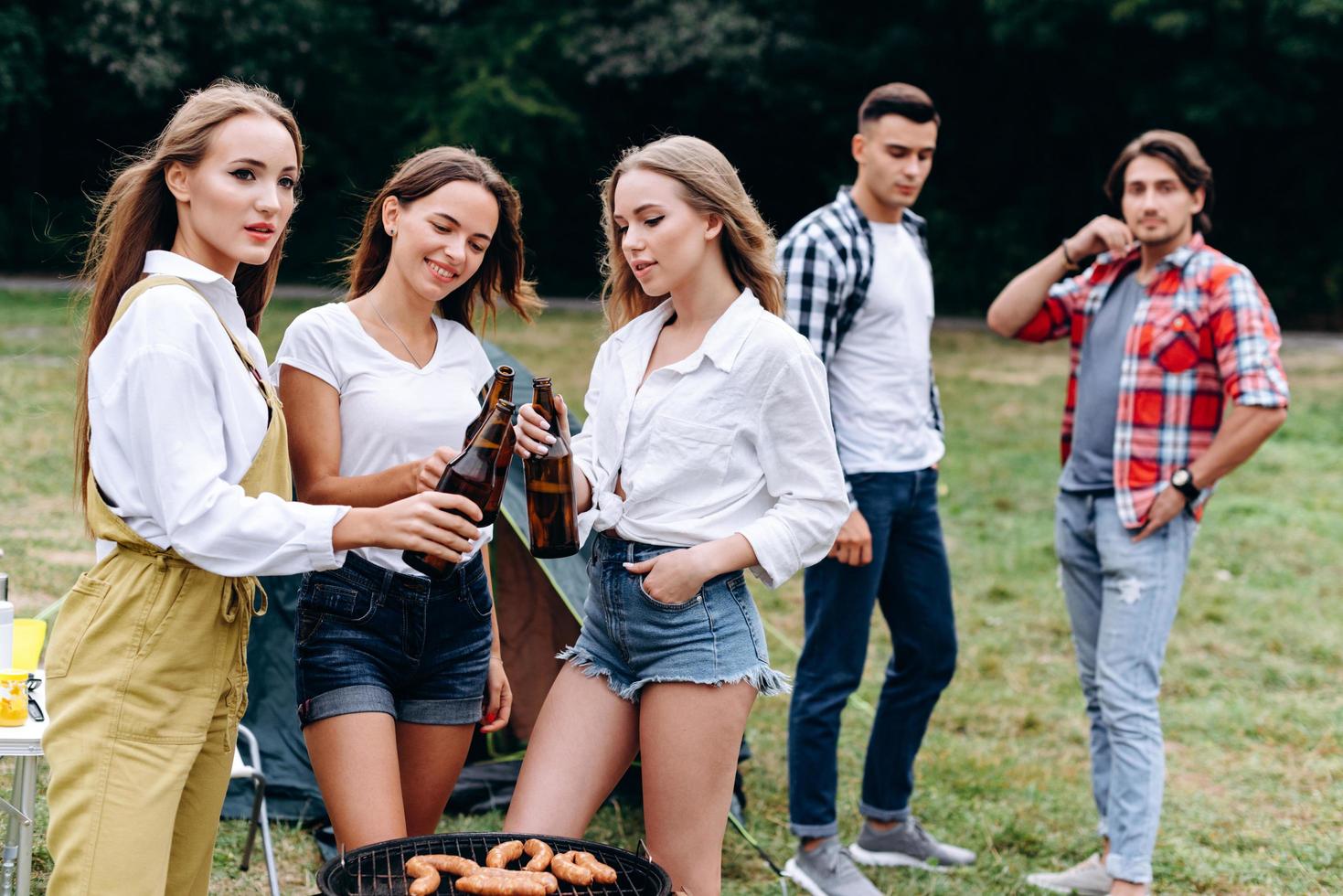 A company of friends raising a bottles with a beer in the camping . - Horizontal image photo