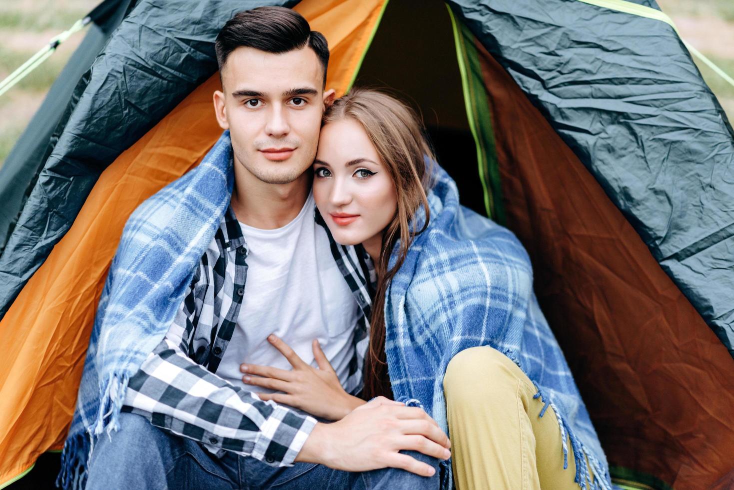 A lovely couple sitting and hugging in the tent outdoor and looking at the camera photo