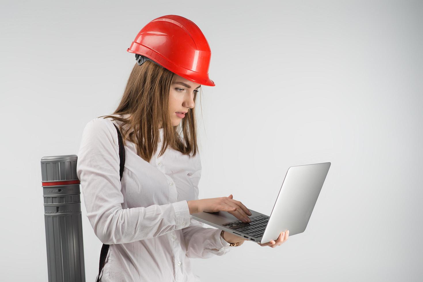 Woman   architect  stands with a tube behind her back holding laptop and looking to the screen photo