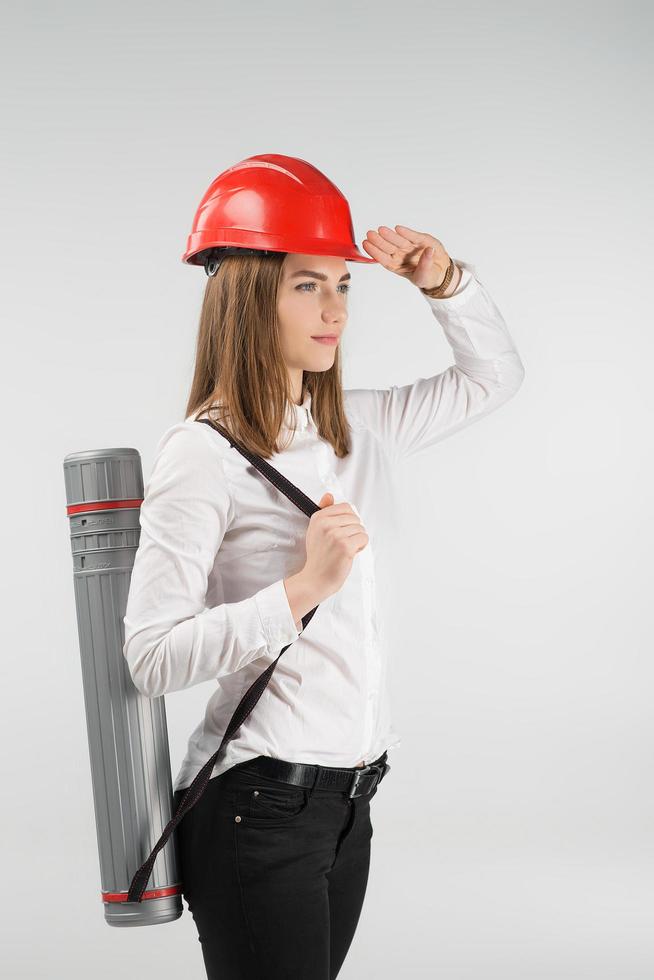 Woman   architect stands with a tube behind her back touches orange helmet on her head. - Vertical image photo