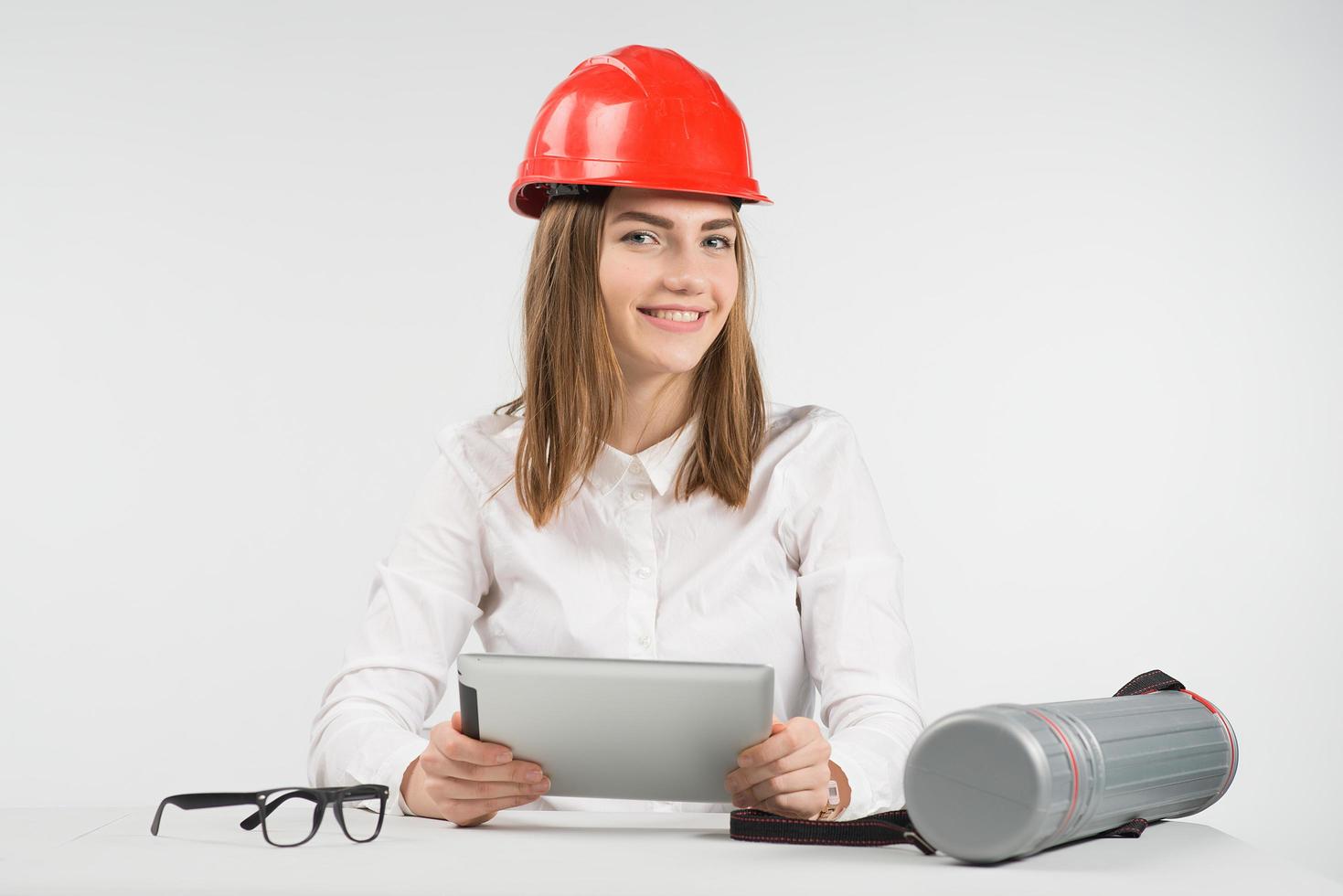 Mujer feliz arquitecto en casco naranja sostiene el ipad y se sienta junto al tubo, gafas foto