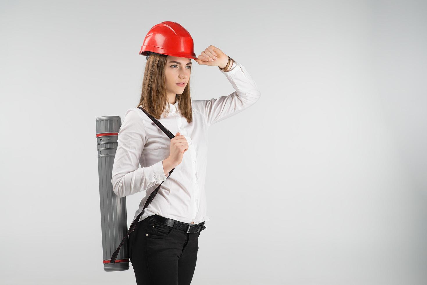 Woman   architect stands with a tube behind her back touches orange helmet on her head. - Horizontal image photo
