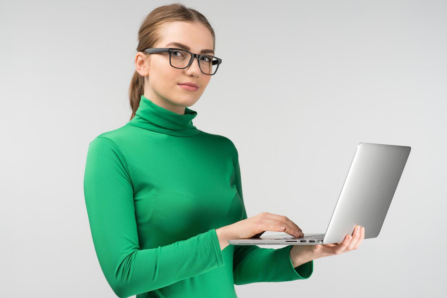 Closeup woman  works on a laptop while standing  in half-turn. Looking  at the camera photo