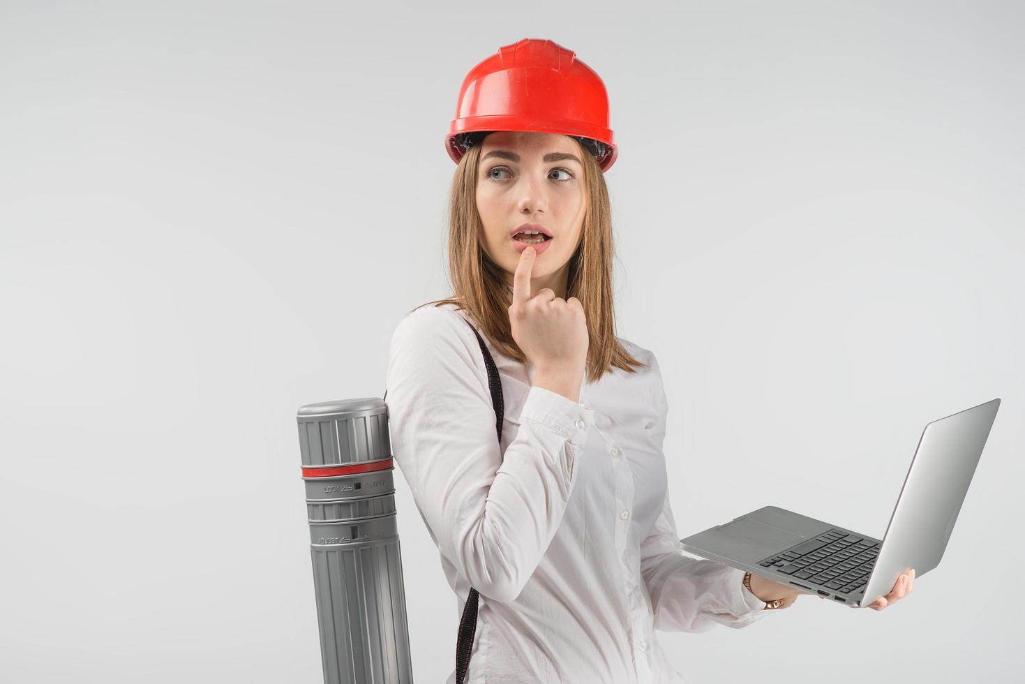 Woman   architect  stands with a tube behind her back holding laptop and looking away lost in thought photo