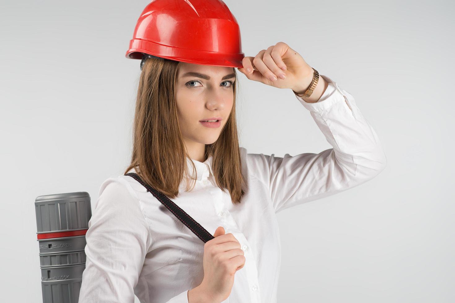 Closeup portrait of pretty woman   architect stands with a tube behind her back touches orange helmet on her head. - Horizontal image photo