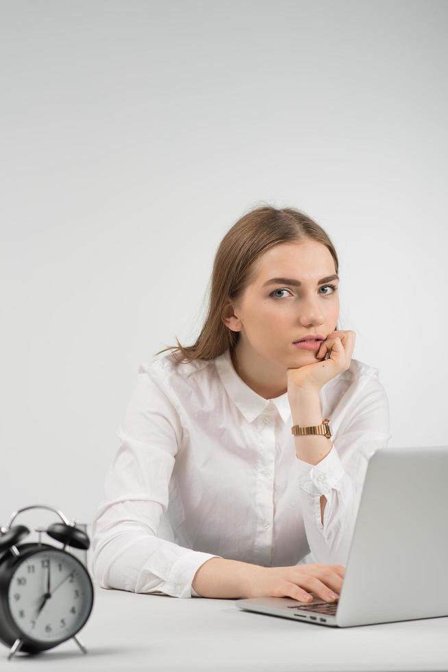 Woman sits at the table and works in laptop looking at the camera photo