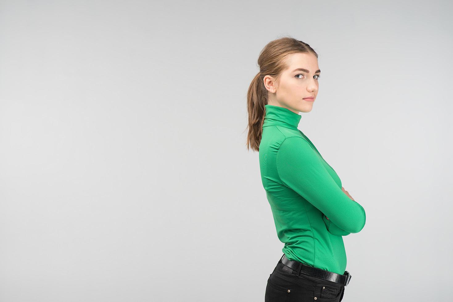 Sideview of a pretty young woman standing with folded arms isolated on the background.  Looking at the camera photo