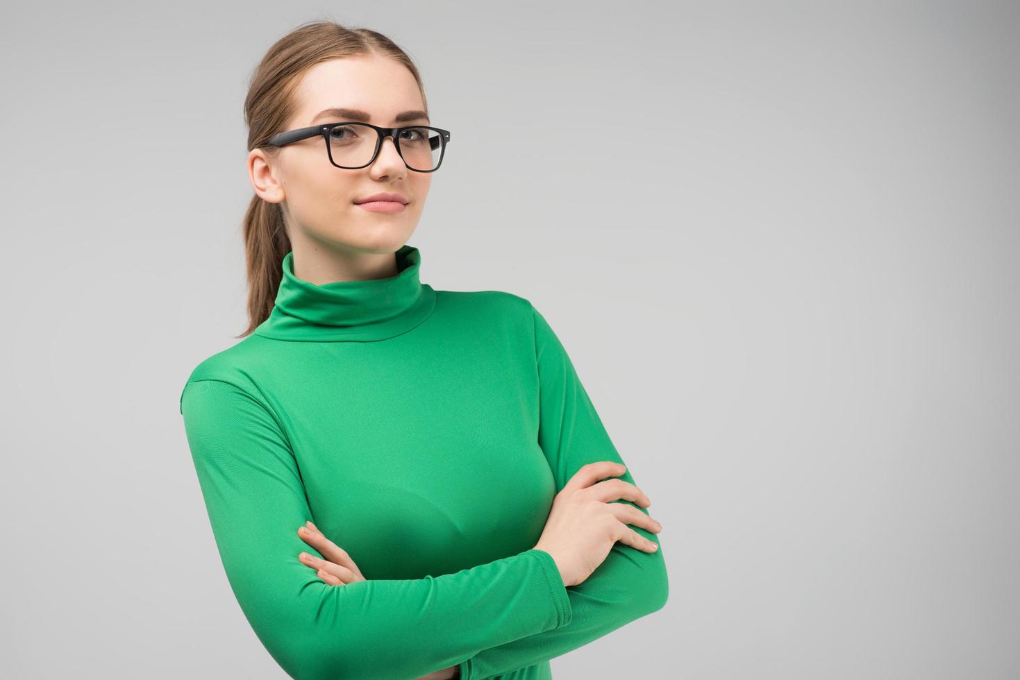 mujer joven seria con gafas y ropa casual posando en el estudio con las manos cruzadas. imagen horizontal foto