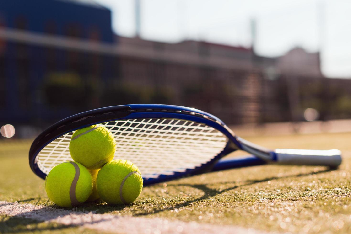 Three tennis balls and racket on hard court under sunlight photo