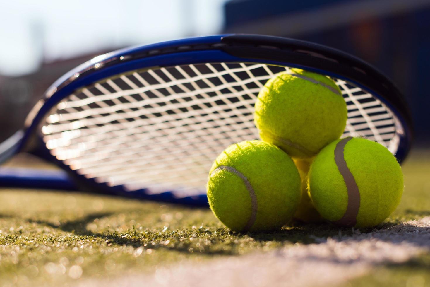 Macro image of three tennis balls and racket on hard court under sunlight photo