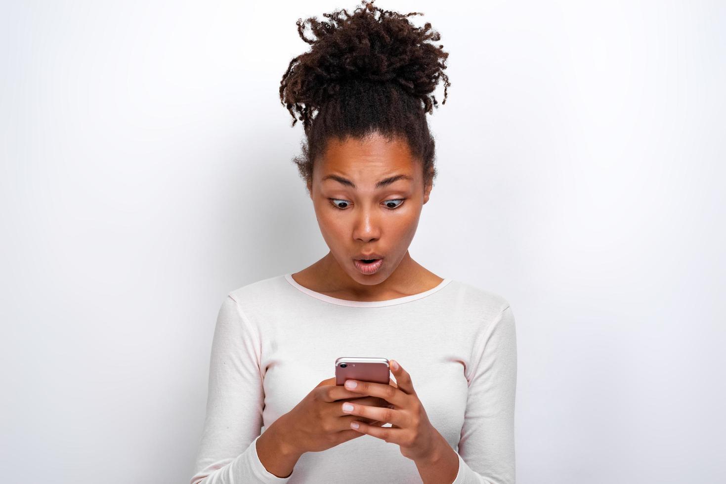 Mujer asombrada sosteniendo un teléfono inteligente en sus manos y conmocionada mirando la imagen de la pantalla foto