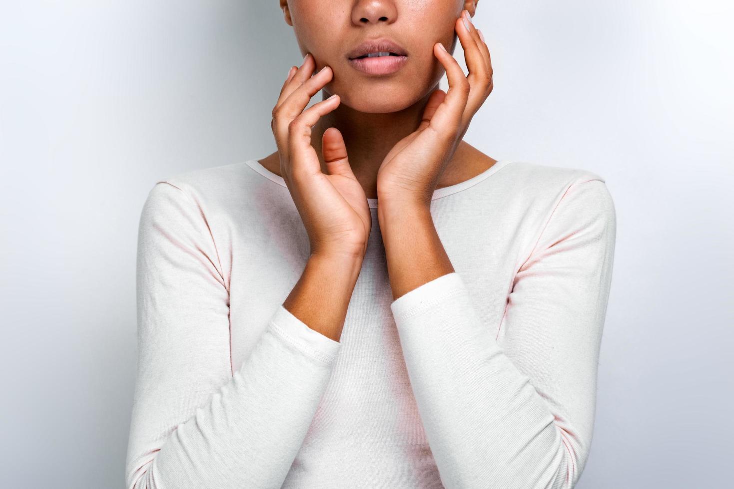 Cropping closeup portrait of a beautiful serious girl over light background touches herself face - Image photo