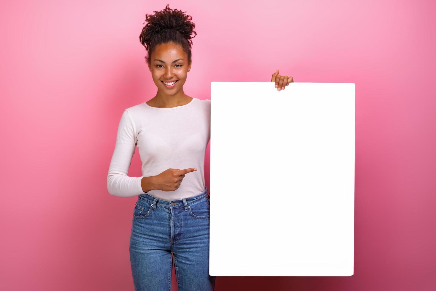 Studio shot of a happy girl pointing for empty white paper sheet copyspace- Image photo