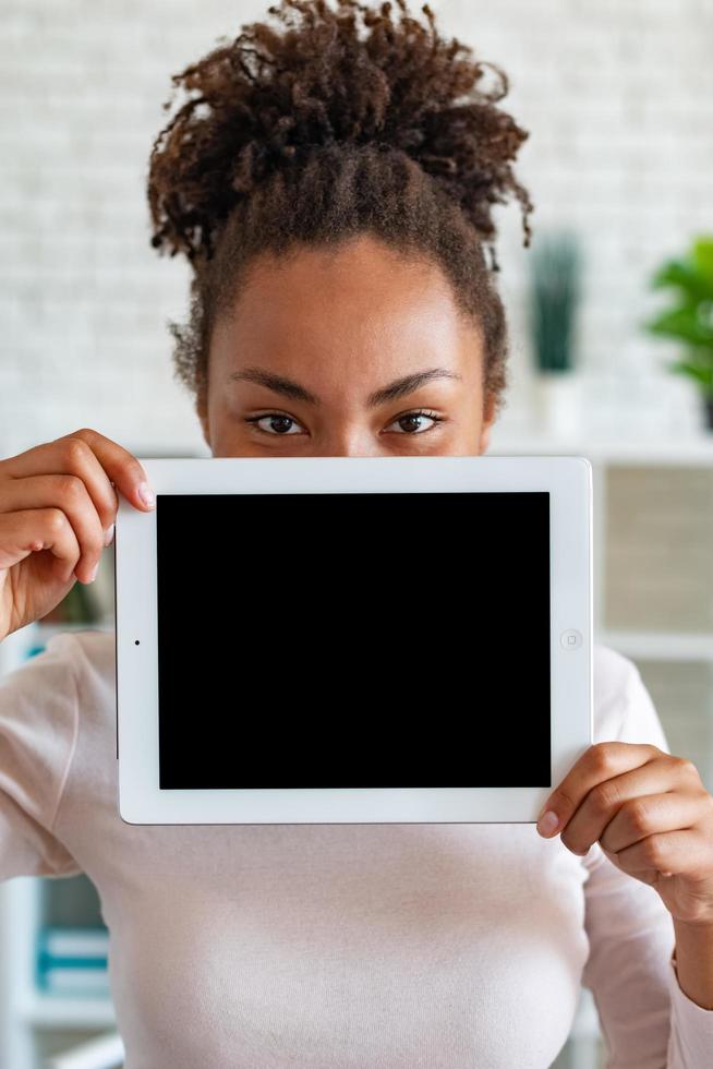 Imagen de maqueta de la pantalla en blanco vacía negra de la tableta en la mano femenina, asomando desde detrás de la tableta foto