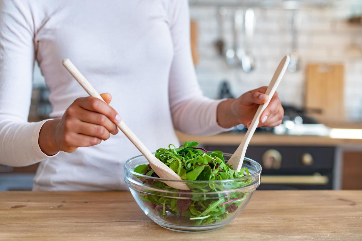 Primer plano de las manos femeninas durante la cocción de un alimento saludable, revuelve con cucharas una ensalada foto