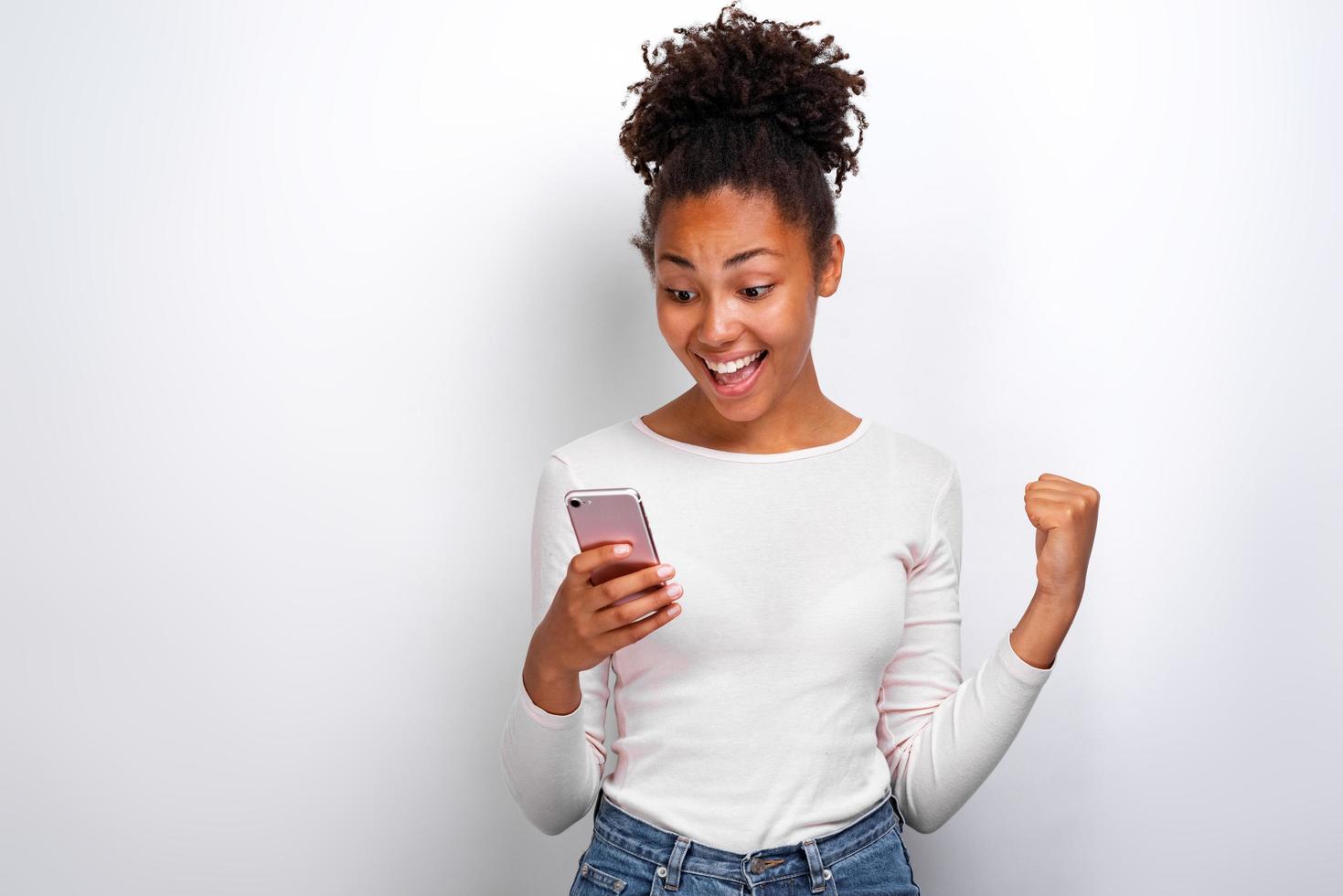 Happy woman holding a smartphone in her hand and screaming with winner gesture looking at the screen photo