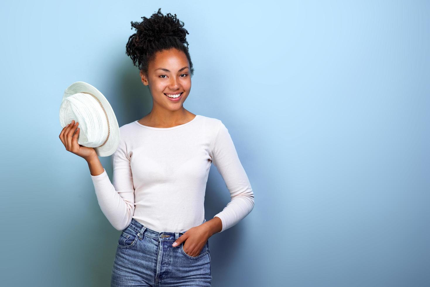 Happy african american traveller woman holds hat and looking at the camera over blue background.- Image photo