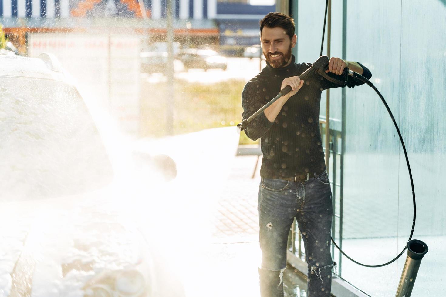 Car wash. Happy caucasian man washing car at the special place. Car wash with high pressure gun concept. Stock photo