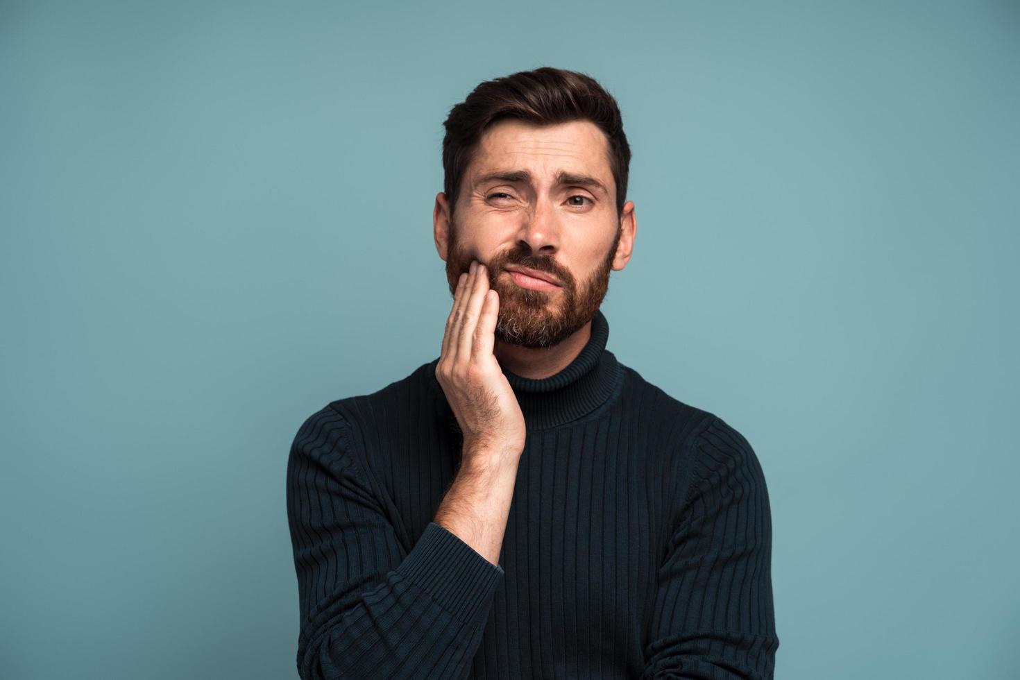 problemas dentales. Retrato de hombre insalubre presionando dolor en la mejilla, que sufre dolor de muelas agudo, enfermedad periodontal, caries o dolor de mandíbula. Foto de estudio de interior aislado sobre fondo azul.