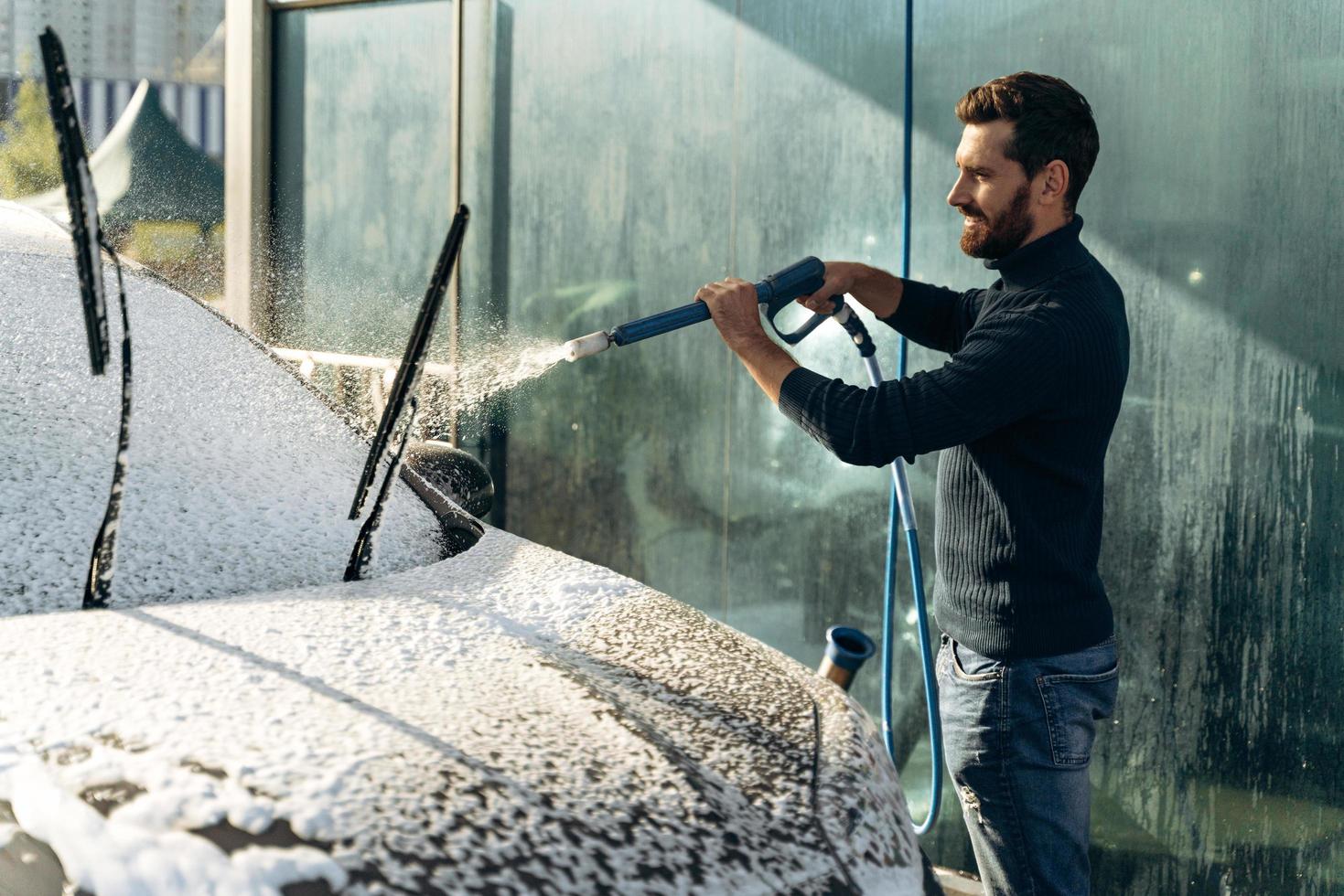 lavado de autos. lavado de autos en el lugar especial solo. hombre sonriendo a la cámara mientras lava el coche negro. Coche de limpieza con concepto de agua a alta presión foto