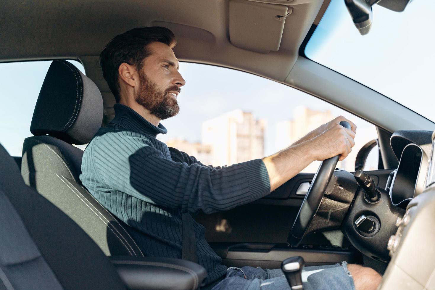 Vista de ángulo bajo del hombre serio confiado en el coche y mirando la carretera durante la conducción. foto de stock