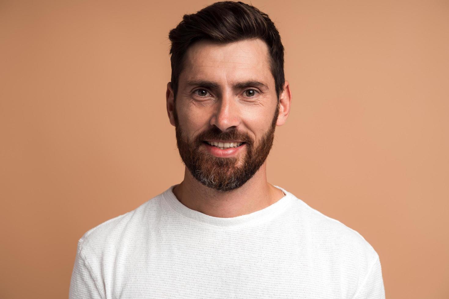 Retrato de hombre guapo alegre con camisa blanca mirando a cámara, sintiéndose con alegría como si tuviera una idea interesante. Foto de estudio aislado sobre fondo beige