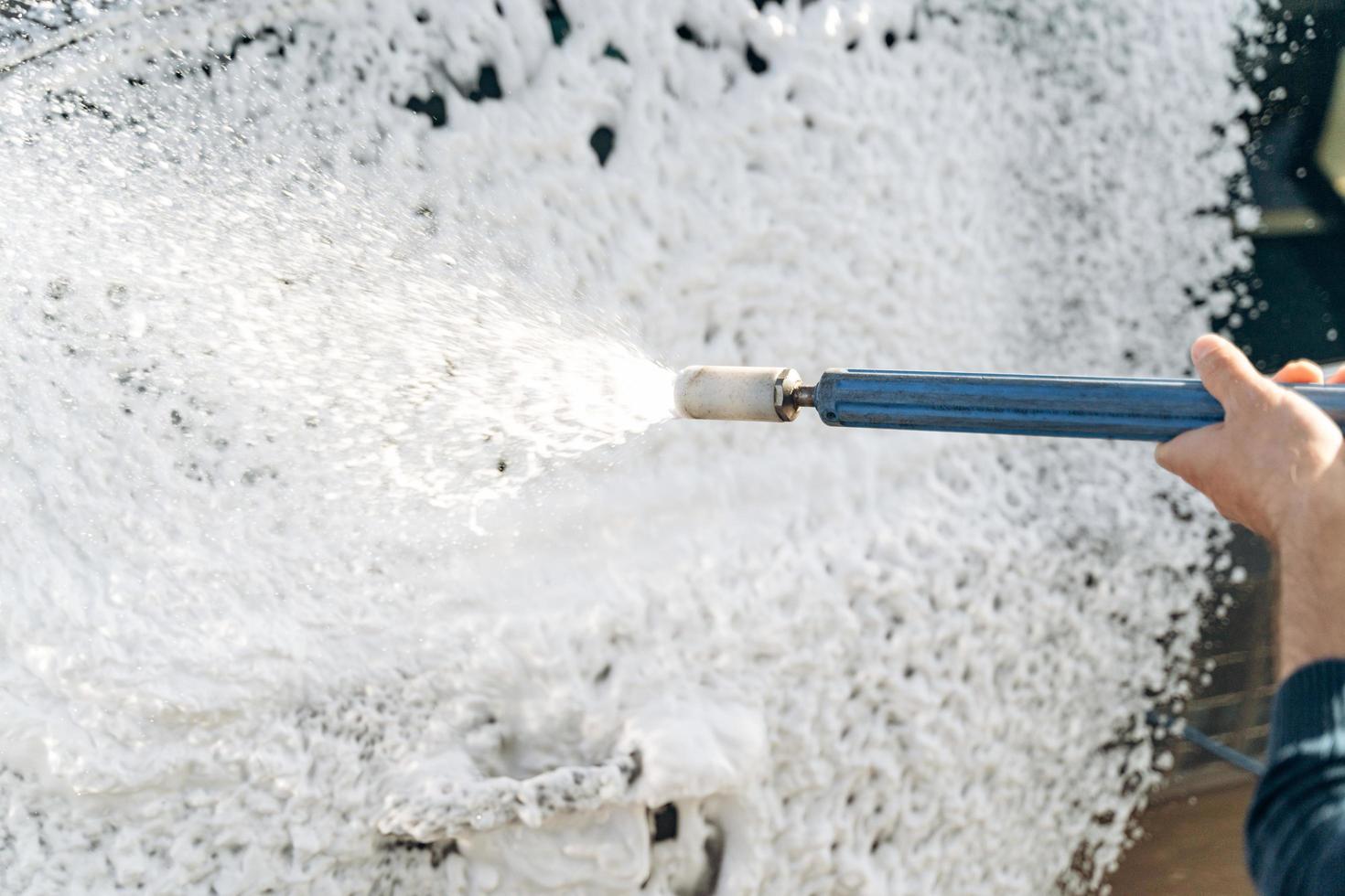 Close up view of the man worker or car owner washing luxury car on a car wash. Manual car washing cleaning with water at service station photo