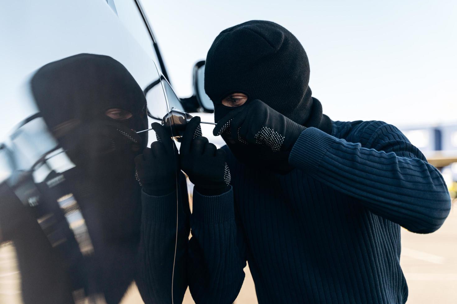 Close up view of the dangerous man dressed in black with a balaclava on his head preparing breaking with crowbar the glass of car before the stealing. Car thief, car theft concept photo