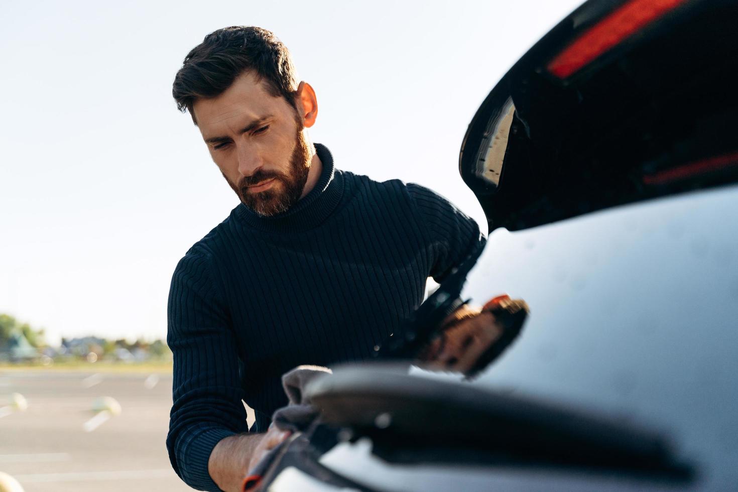 Foto de un hombre concentrado satisfecho limpiando la carrocería de su coche mientras pasa tiempo en la calle durante el día soleado de verano. foto de stock