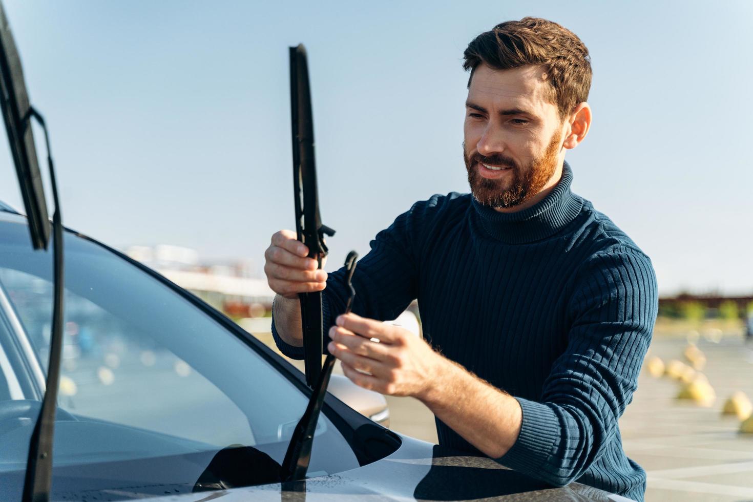 propietario de automóvil masculino comprobando el limpiaparabrisas en la calle. El hombre está cambiando los limpiaparabrisas de un automóvil. concepto de reparación de automóviles foto