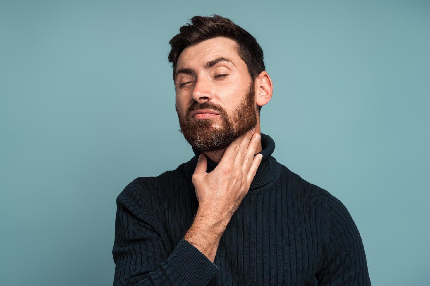 infeliz enfermo tocando el cuello sintiendo dolor al tragar, resultado de asfixia, inflamación de garganta, dolor de garganta. Foto de estudio de interior aislado sobre fondo azul.