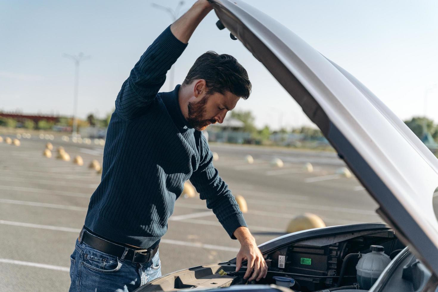 Cerca del hombre con un problema de coche. hombre confundido en un cierre casual examina el motor del coche mientras está de pie en la carretera. foto de stock