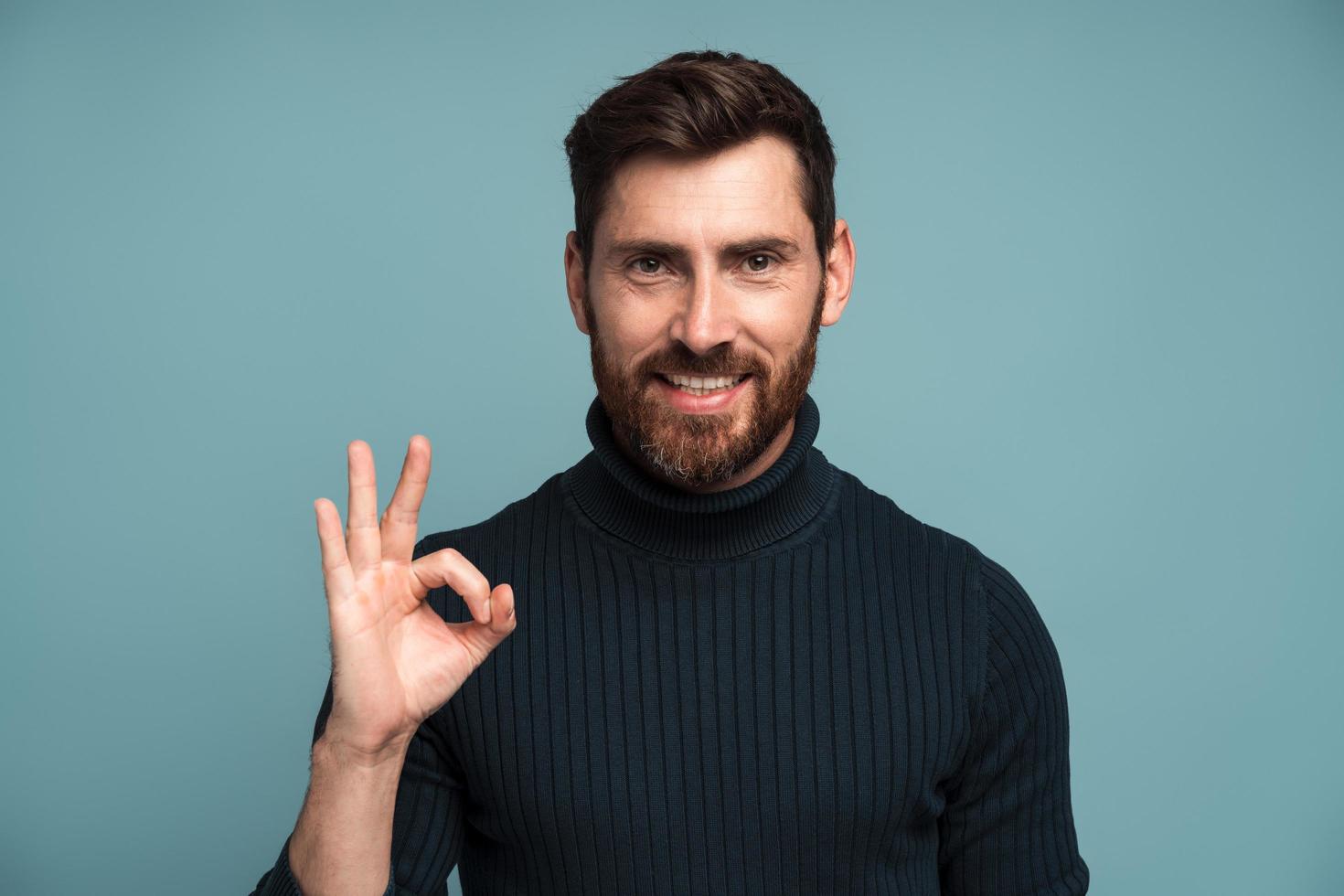 Everything is fine. Satisfied bearded man boss showing ok gesture with fingers, approving work, satisfied with quality. Indoor studio shot isolated on blue background photo