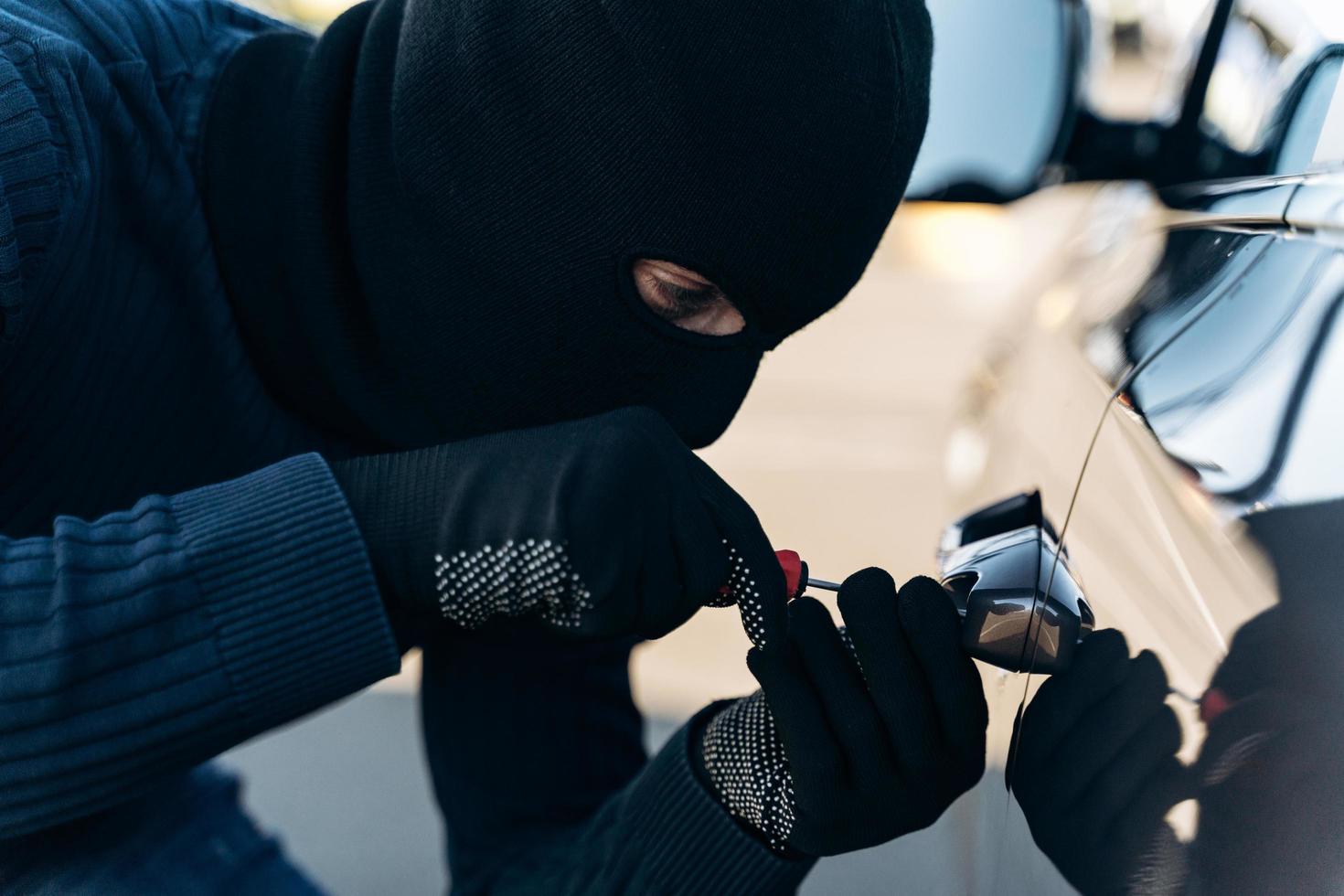 Vista de cerca del peligroso hombre vestido de negro con un pasamontañas en la cabeza que abre la cerradura con una ganzúa mientras roba. ladrón de autos, concepto de robo de autos foto