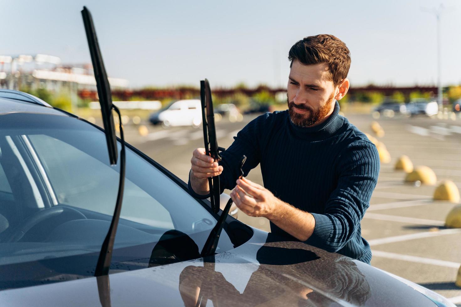 El hombre está cambiando los limpiaparabrisas de un automóvil mientras está de pie en la calle. macho reemplace los limpiaparabrisas del coche. Cambiar concepto de escobillas de limpiaparabrisas de coches foto