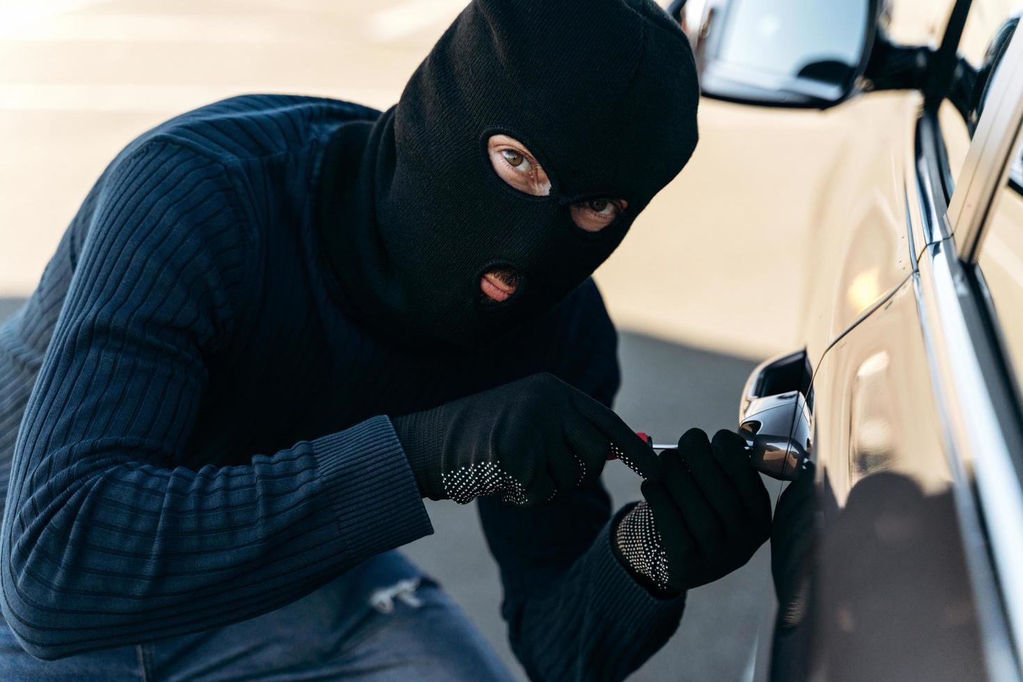 Vista de cerca del peligroso hombre vestido de negro con un pasamontañas en la cabeza que abre la cerradura con una ganzúa mientras roba. ladrón de autos, concepto de robo de autos foto