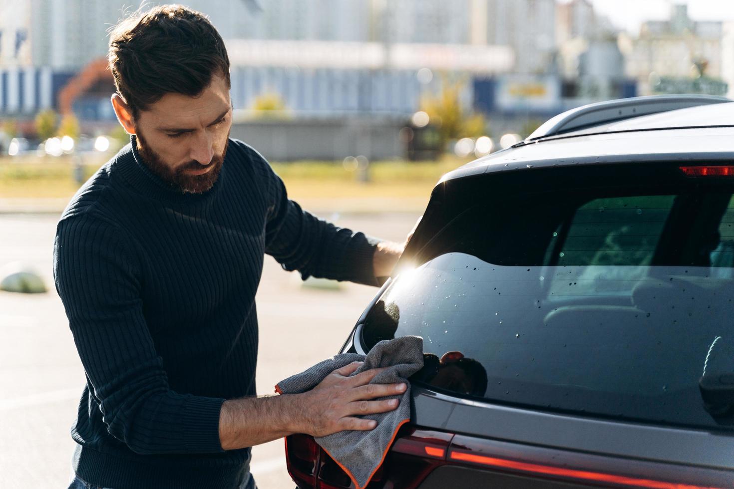 Waist up portrait view of a satisfied concentrated man cleaning the back of his new car while spending time at the street during the sunny summer day. Stock photo