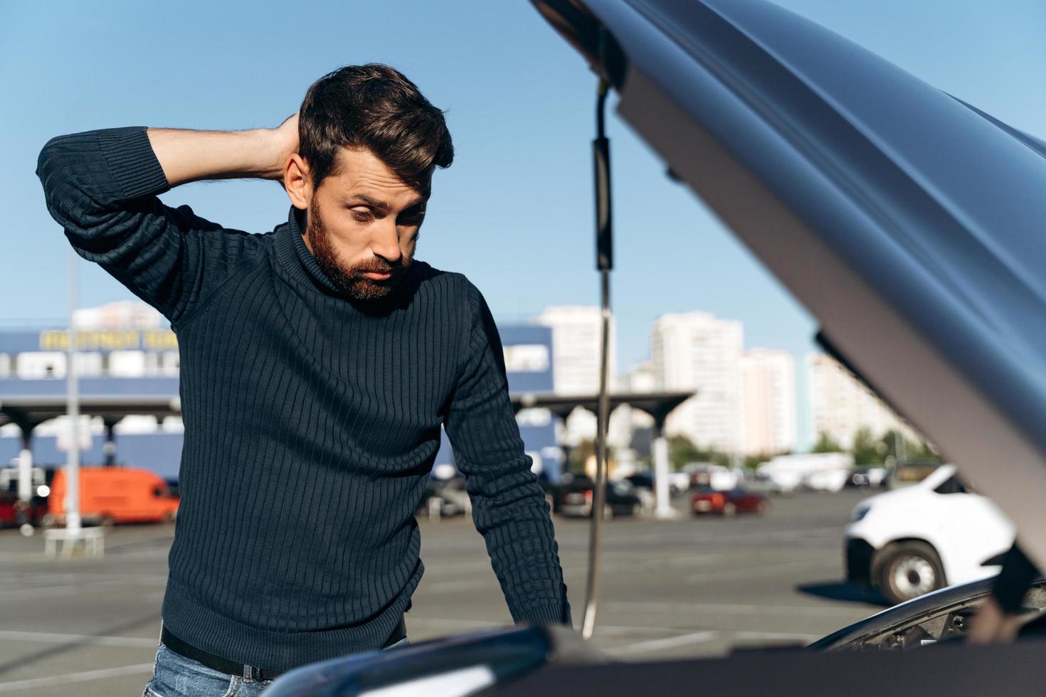 El hombre desconcertado que mira la sala de máquinas de su automóvil parece tener una condición anormal. chico pensando qué hacer. concepto sobre seguro de coche foto