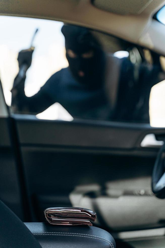 Vertical view from the car at the man dressed in black with a balaclava on his head preparing breaking with crowbar the glass of car before the stealing. Car thief, car theft concept photo