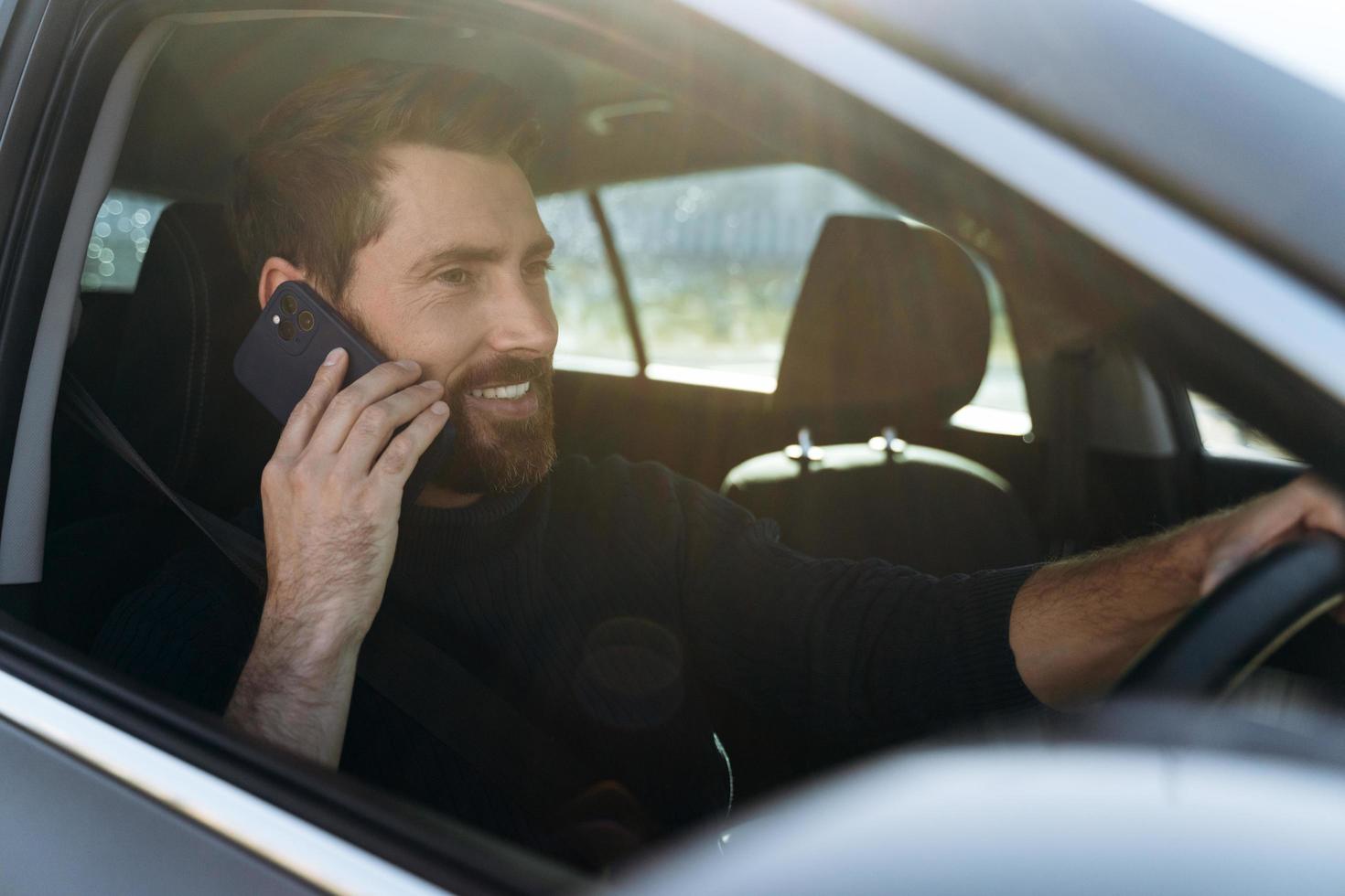 en la carretera. Vista vertical del hombre caucásico consciente mirando por la ventana mientras charla a través del teléfono inteligente con su colega durante el largo camino hacia el trabajo foto