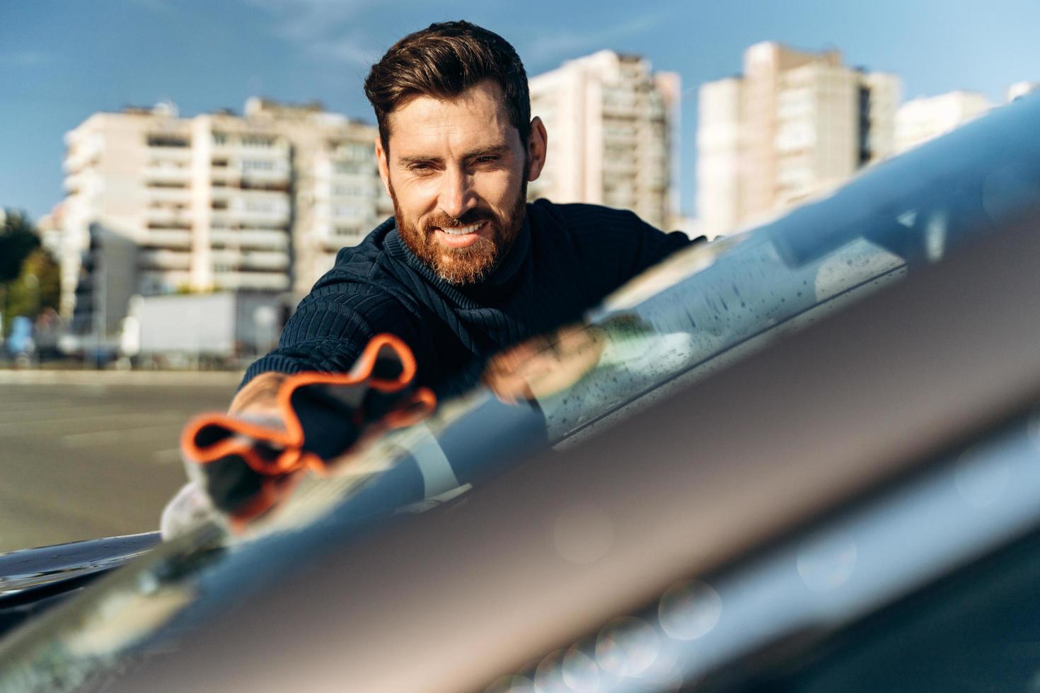 Hand wipe down paint surface of shiny car after polishing. Smiling man cleaning car and drying vehicle with microfiber cloth. Car detailing and car wash concept photo