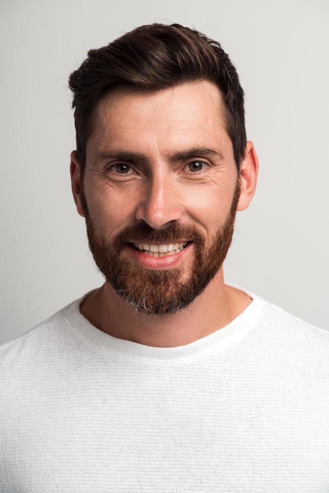 Vertical portrait of happy handsome bearded man standing and smiling cheery to the camera. Indoor studio shot, isolated on white background photo