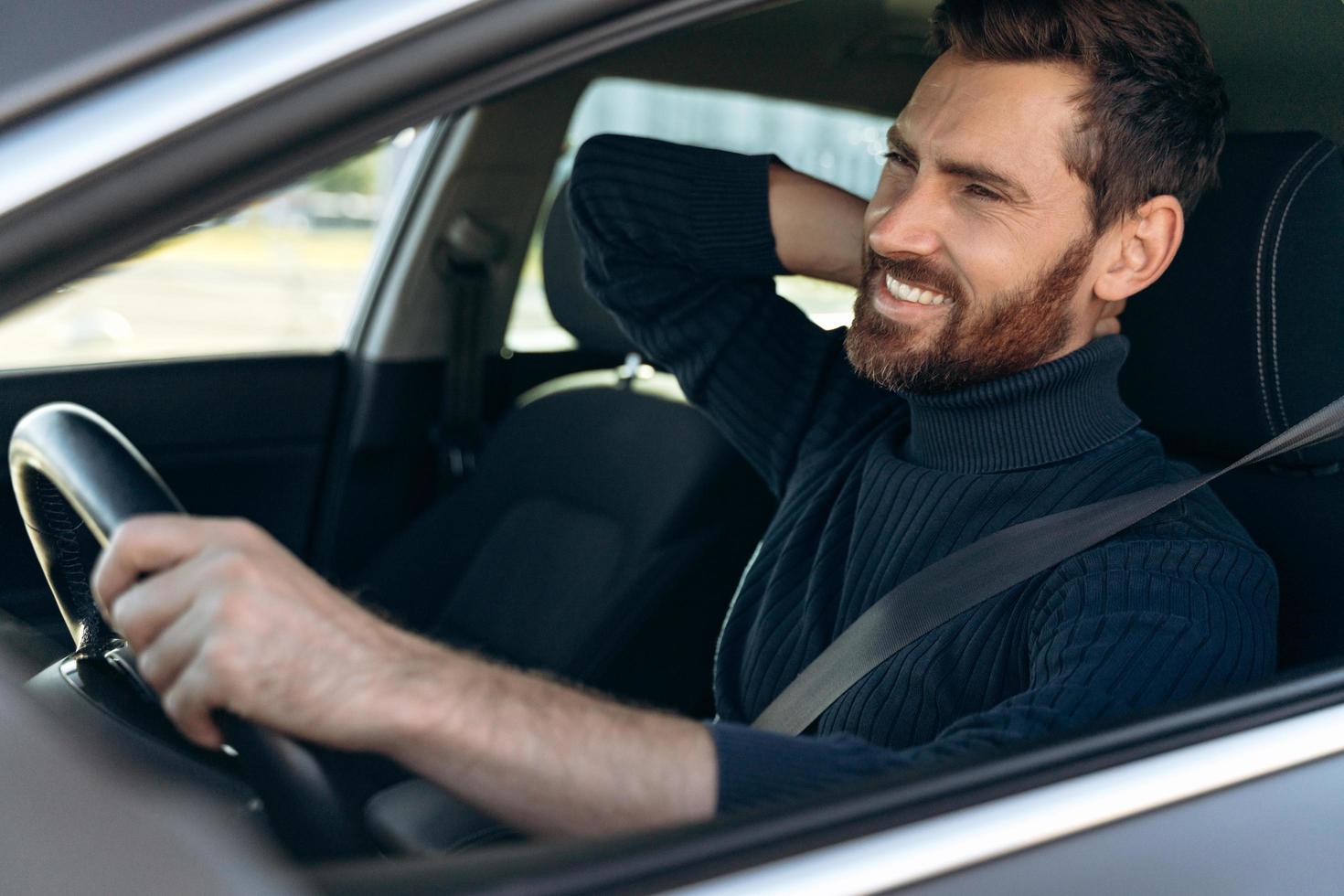 Vista desde la calle del joven frotándose el dolorido cuello, mientras se veía cansado de conducir. conductor masculino que tiene dolor de cuello, sentado en su coche foto