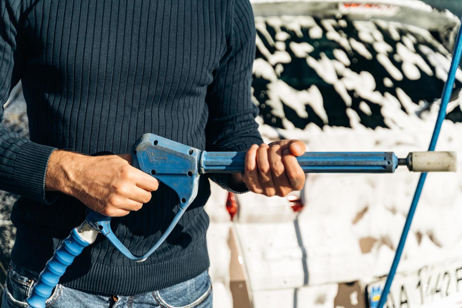 Close up view of the handsome young man holding high pressure gun while preparing to spraying at his car during the cleaning. Stock photo