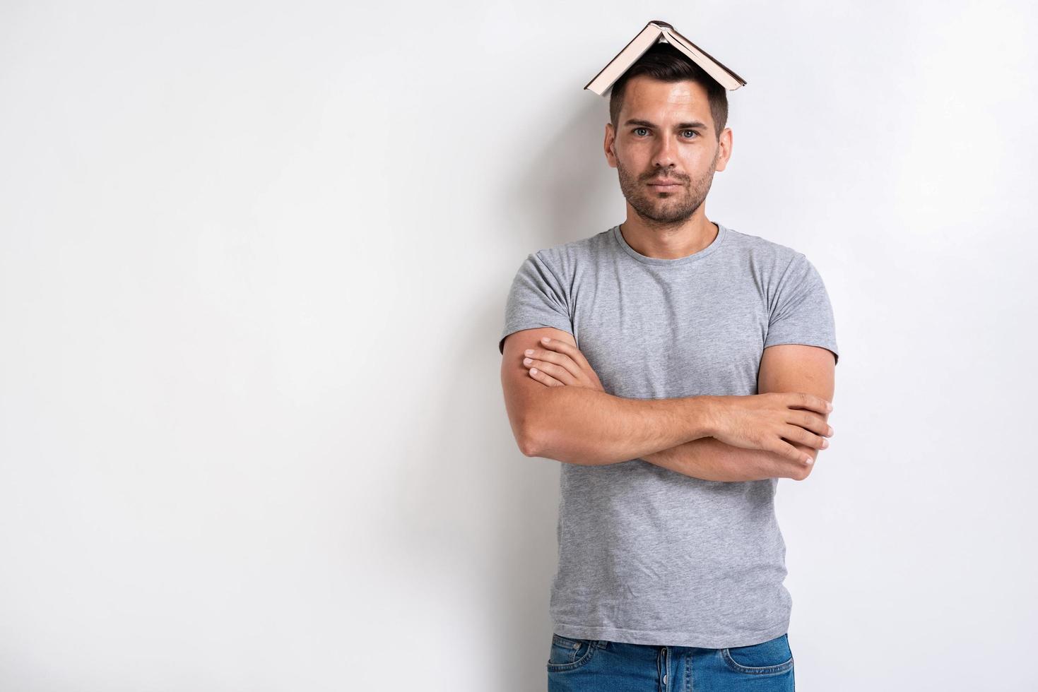 Serious man with book on his head standing folded hands and looking at the camera.- Image photo