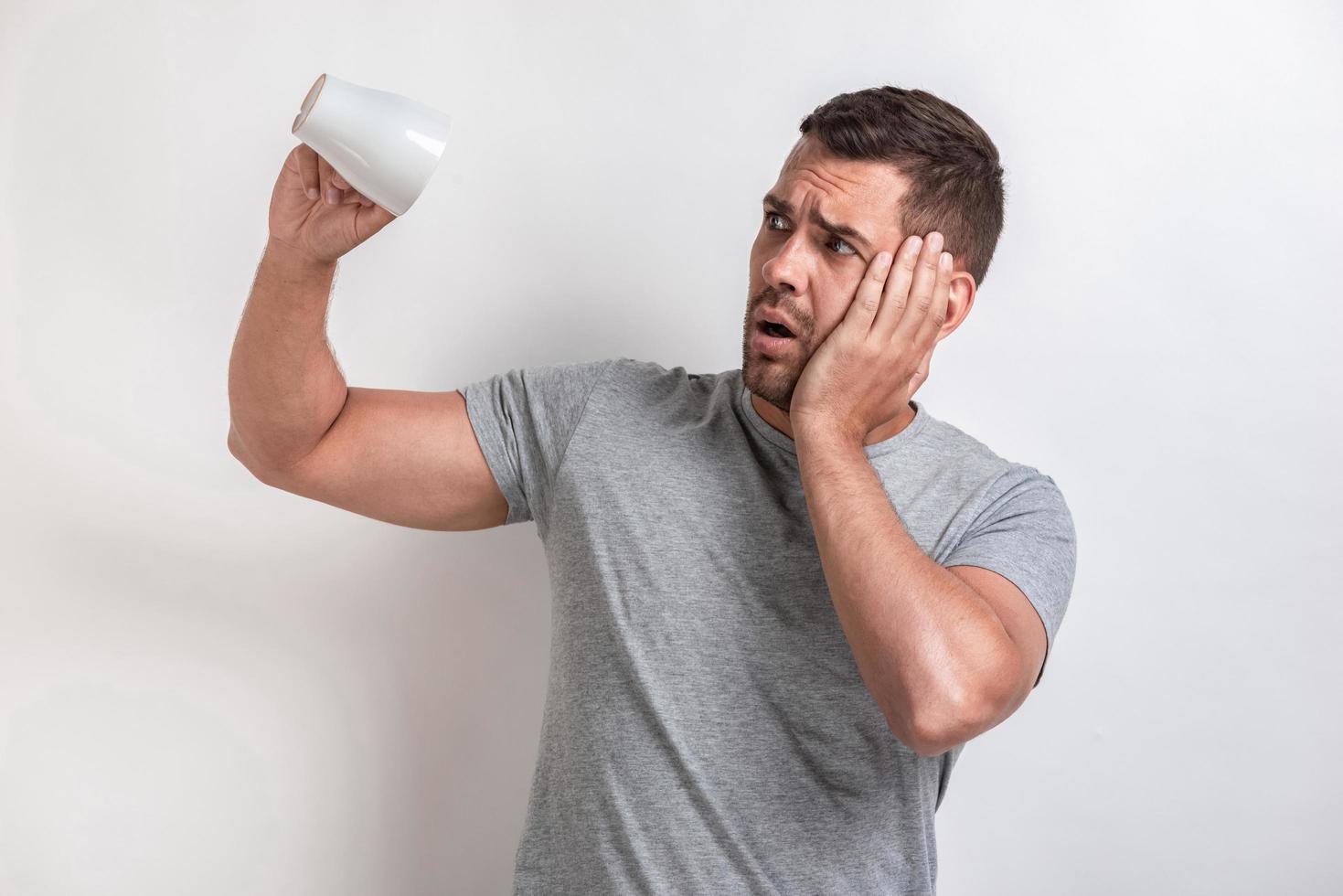 Sadly man flips an empty cup and looking unhappy, touches on cheek.- Image photo